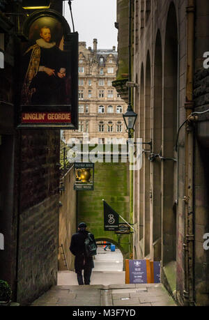 Hombre caminando en el estrecho callejón con Jinglin Fleshmarket Geordie y Halfway House pub signos, Edimburgo, Escocia, Reino Unido, con el Balmoral Hotel en distancia
