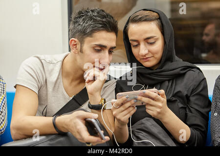 Teherán, Irán - Abril 28, 2017: una joven pareja iraní utiliza dispositivos móviles mientras viajaba en un vagón de metro. Foto de stock