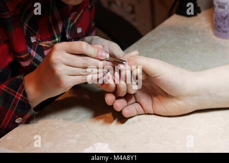 Un estudiante en los cursos de capacitación de una manicura da forma a las uñas de la mano de un hombre con un cliente para eliminar cutículas superfluas y pterigión. Foto de stock