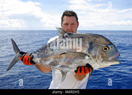 Pesca en mar profundo - Feliz pescador sosteniendo un trevally jack Foto de stock