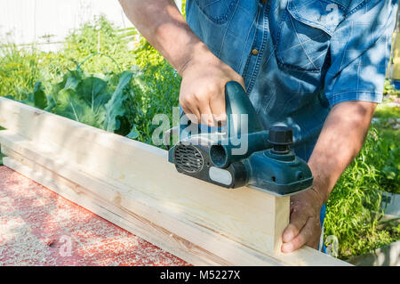 El maestro agudiza el panel de madera con una lijadora eléctrica en un día  soleado en el jardín. El peligro. Infracción de las normas de seguridad  Fotografía de stock - Alamy