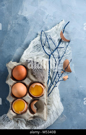 Adornos de Pascua concepto con huevos frescos en una caja de cartón, ramas de árboles y trapo corredor sobre un fondo de hormigón. Vista superior con espacio de copia.