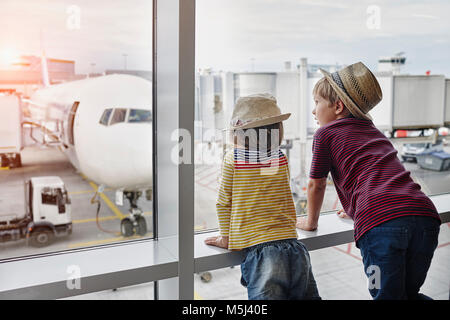 Dos niños usando sombreros de paja mirando a través de la ventana de avión en el delantal