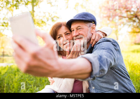 Las parejas ancianas con smartphone fuera en la primavera de la naturaleza.