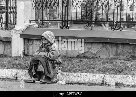 Una mujer sentada en la carretera cerca del parque y pide dinero. Fotografía en blanco y negro. Foto de stock