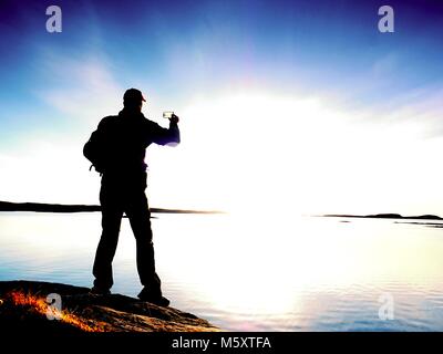 Silueta de hombre conservar recuerdos con la cámara del teléfono en su mano. Maravillosa puesta de sol en el mar, buen nivel de agua