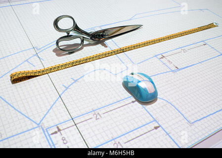 Proyección de un patrón para una chaqueta de papel sobre una mesa en un taller sastres con un ratón de ordenador, cinta métrica y cizallas o tijeras Foto de stock