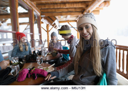 Retrato sonriente, seguro joven esquiador comiendo con la familia apres-ski en ski resort lodge balcón