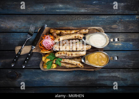 Salchichas asadas con chucrut, mostaza y las rodajas de patata. servida con cubiertos de madera en el fondo, vista desde arriba. Foto de stock