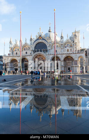 La Basílica de San Marcos se refleja en acqua alta en Piazza San Marco, la Plaza de San Marcos, San Marco, Venecia, Véneto, Italia en un día soleado con el cielo azul.