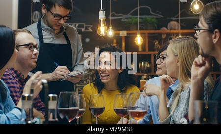 En el Bar/Restaurante El camarero toma el orden de un diverso grupo de amigos. Bellas personas beben vino y tener un buen tiempo en este elegante lugar.