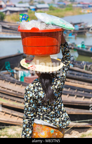 Mujer llevando compras en balde equilibrado en cabeza en el mercado de cinco días Nam Pan, Lago Inle, Estado de Shan, Myanmar (Birmania), Asia en febrero