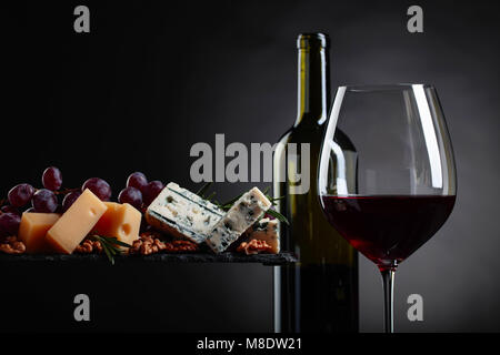 Vaso de vino tinto con distintos quesos, uvas y nueces sobre un fondo negro.Copia espacio .