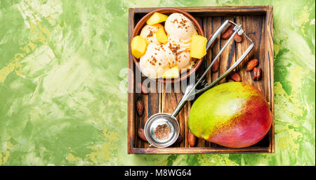 Helado de mango, fruta y una cuchara para helado en bandeja de madera Foto de stock
