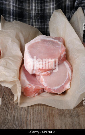 Un montón de filetes de cerdo cruda picada fresca sobre los huesos en envoltura de papel en las manos de un hombre Foto de stock