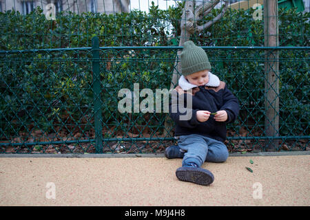 Muchacho sentado en el piso, solo en el patio de recreo, buscando vulnerables Foto de stock