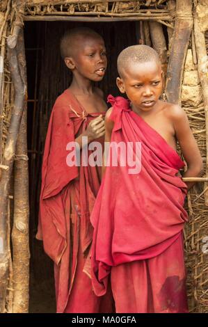 Los niños masai a la entrada de sus chozas en un tradicional pueblo Massai, Kenya. Foto de stock