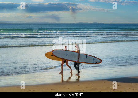Los surfistas caminando por la playa al paso, Byron Bay, New South Wales, Australia Foto de stock