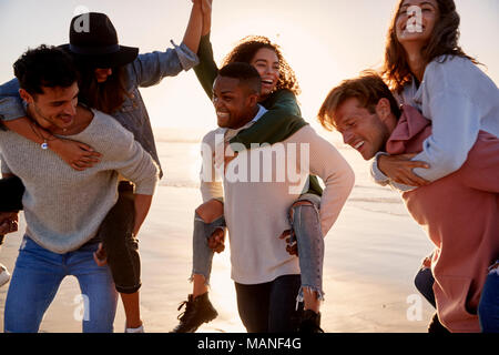 Grupo de Amigos que Piggyback Carrera en invierno junto en la playa Foto de stock