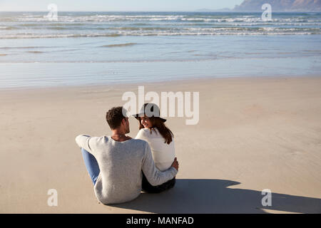 Pareja romántica sentado en la playa de invierno juntos