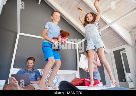 Niños entusiasmados saltar en la cama como padres Pack para vacaciones Foto de stock