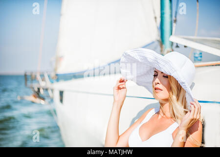 Hermosa chica en traje de baño blanco y un sombrero de ala ancha cerca de  un velero en el mar Fotografía de stock - Alamy