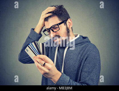 Confundirse destacado hombre mirando demasiadas tarjetas de crédito de la deuda completa