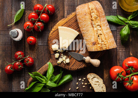 Comida italiana, queso parmesano, pan ciabatta, Bruschetta, tomates y albahaca sobre fondo de madera rústica. Vista superior