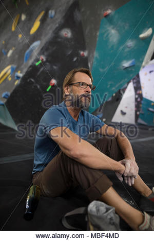 Centrado macho maduro escalador descansando debajo de muro de escalada en el gimnasio de escalada