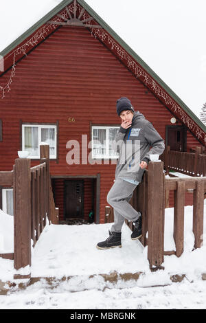 Traveller boy fumar piscina en frente de la casa de madera en invierno. Snowboarder lifestyle Foto de stock