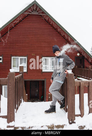 Traveller boy fumar piscina en frente de la casa de madera en invierno. Snowboarder lifestyle Foto de stock