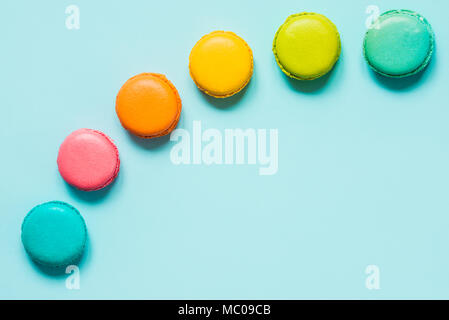 Coloridos macarons dispuestos como arco iris sobre fondo azul.