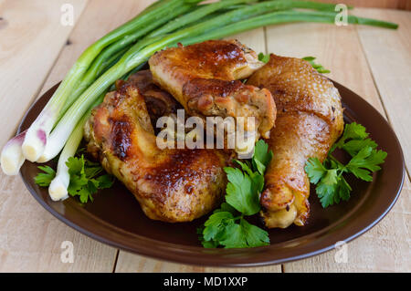 Asado jugoso pollo (piernas, aletas) sobre una placa de arcilla sobre un fondo de madera ligera