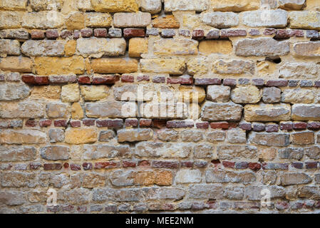 Fondo de patrón irregular de color amarillento, rojo y gris grunge capeado ladrillos irregulares en la superficie de una pared de piedra Foto de stock