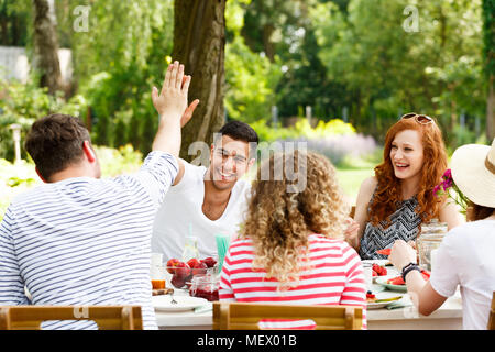 Sonriente, grupo de jóvenes divirtiéndose, riendo y comiendo alimentos sanos fuera Foto de stock