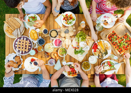 Grupo de estudiantes en un picnic comer pizza, pasteles, frutas y verduras en el jardín Foto de stock