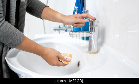 Foto en primer plano de una joven empapando una esponja amarilla con agua antes de hacer la limpieza en el baño. Foto de stock