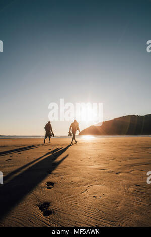Canadá, Columbia Británica, Vancouver Island, dos hombres caminando en la playa en la Bahía de San Josef al atardecer Foto de stock