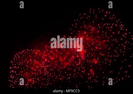 Fuegos artificiales y humo en color rojo contra un cielo negro como fondo.