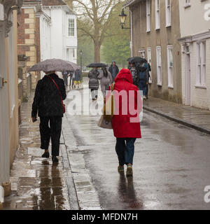 Gente caminando con un paraguas durante una pesada lluvia de Abril ducha en la entrada a la Catedral, cerca de Salisbury, Wiltshire, UK Foto de stock