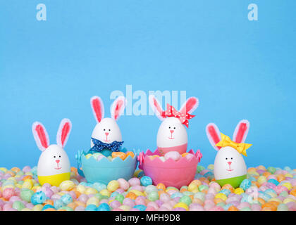 Conejitos de Pascua artesanales hechas de plástico dos huevos en cestas llenas de golosinas con dos de pie en pastel Jelly Beans con un fondo de color azul claro. Diversión Eas Foto de stock