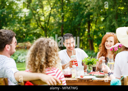 Los jóvenes riendo, comiendo y hablando en un día soleado en el jardín Foto de stock