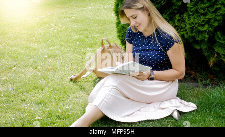 Retrato de joven mujer rubia sentado bajo el árbol del parque ar y escribir en diario Foto de stock