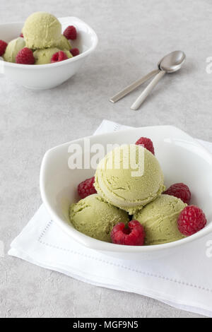 Cucharadas de matcha orgánico casero helado y frambuesas frescas en dos tazones de porcelana blanca sobre fondo gris fondo de textura. Foto de stock