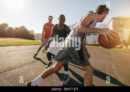 Hombres jugando juego de baloncesto en un día soleado. Los hombres que practicaban el baloncesto habilidades en el área de juego. Foto de stock
