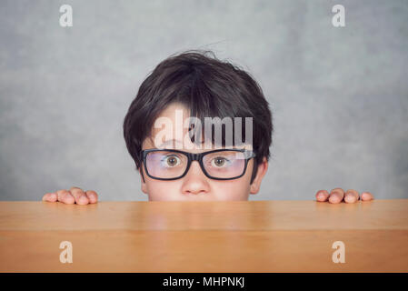 Niño con gafas sobre una tabla de madera sobre fondo gris Foto de stock