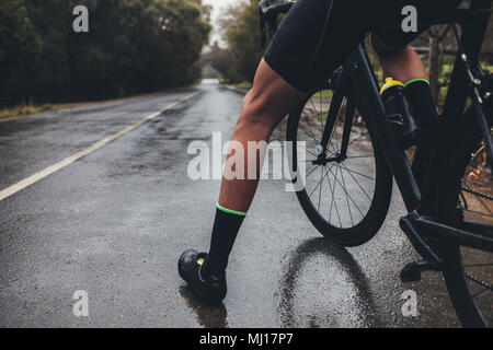 Bajo la sección Foto de atleta masculino de pie con su bicicleta. El hombre ciclista con su bicicleta de carretera mojada. Captura recortada de triatleta masculino con su cy