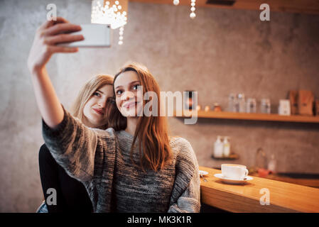 Dos amigos tomando café en una cafetería, teniendo selfies con un teléfono inteligente y divertirse haciendo muecas. Centrarse en la chica de la izquierda
