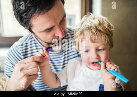 Padre cepillar sus dientes con un niño chico en casa. Foto de stock