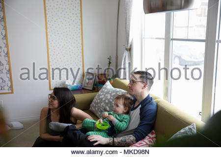 Joven familia comiendo, viendo la televisión en la sala de sofá